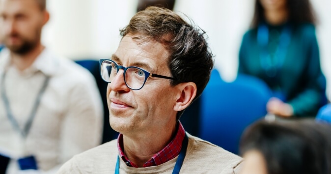 A man with glasses in a room full of people looking off camera.