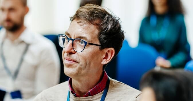 A man with glasses in a room full of people looking off camera.