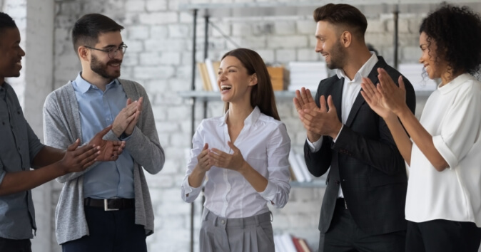Group of people clapping for a woman demonstrating how to make employees feel valued and appreciated.
