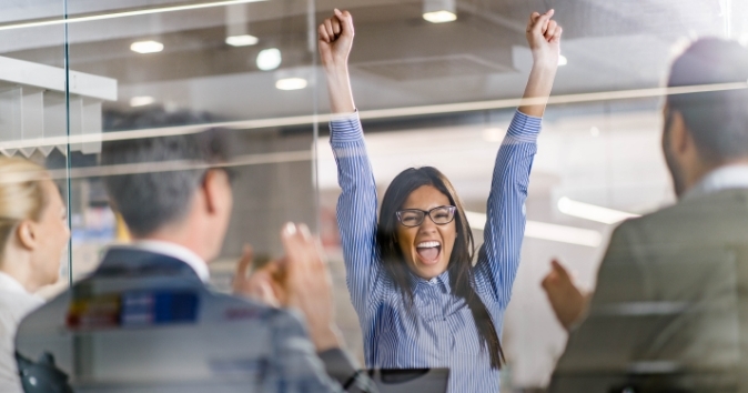 A woman in a meeting is throwing her hands up, celebrating.