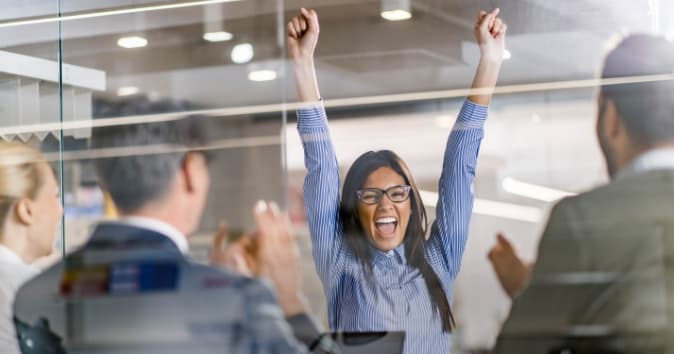 A woman in a meeting is throwing her hands up, celebrating.