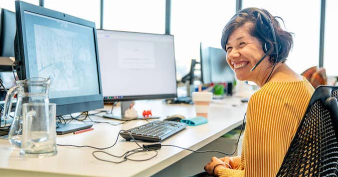 Women sitting at the office desk wearing headphones and smiling