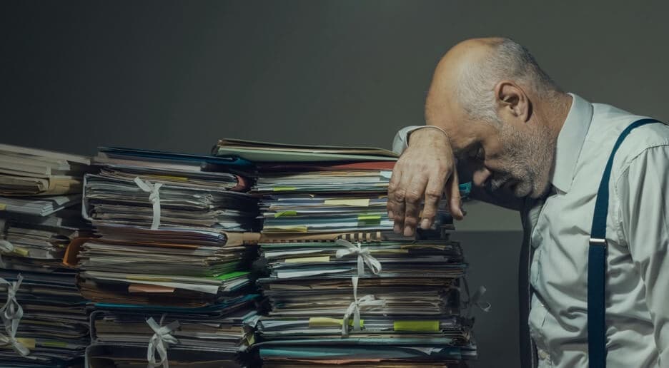 Man resting head on stacks of paperwork