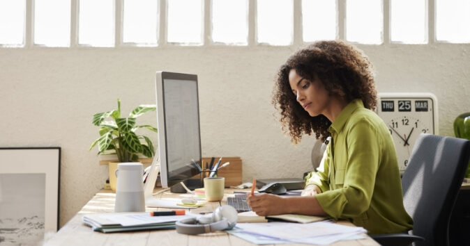Woman at home office writing on a notepad exemplifying remote work diversity.