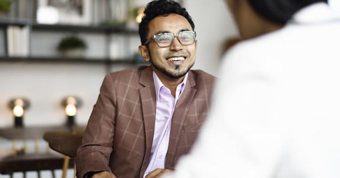 a person sitting at the table wearing specs and smiling