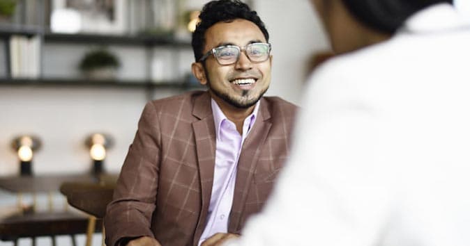 a person sitting at the table wearing specs and smiling