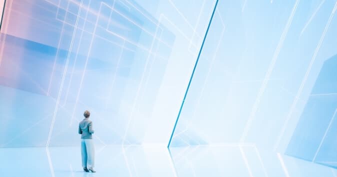 A person wearing a light gray suit stands with their back to the camera, gazing at a bright and abstract futuristic environment, reflecting on what is the future of work. The setting features soft, smooth surfaces with a pale blue and pink color palette and geometric lines that create a sense of depth and modernity. The atmosphere suggests a blend of technology and imagination, evoking feelings of exploration and potential.
