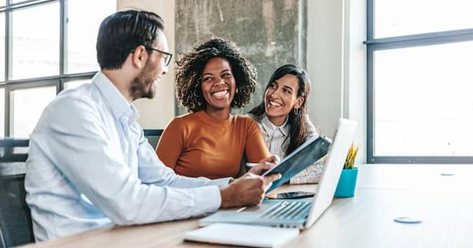 Employees sitting at the desk discussing and smiling.
