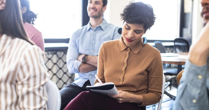 Woman taking notes in an office meeting about areas of growth and development for employees.