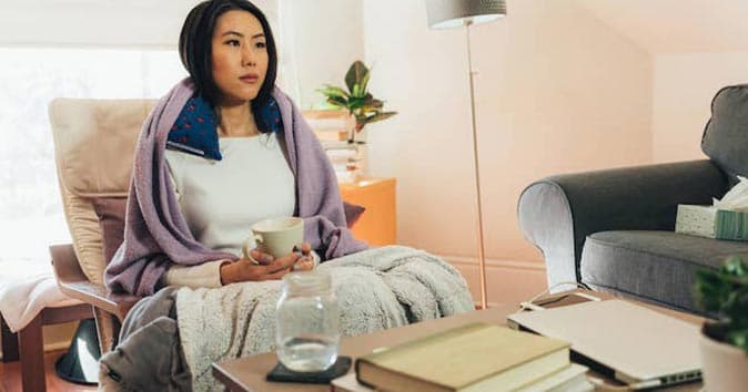 Women sitting on the sofa covered in blankets, holding a coffee cup in hand.