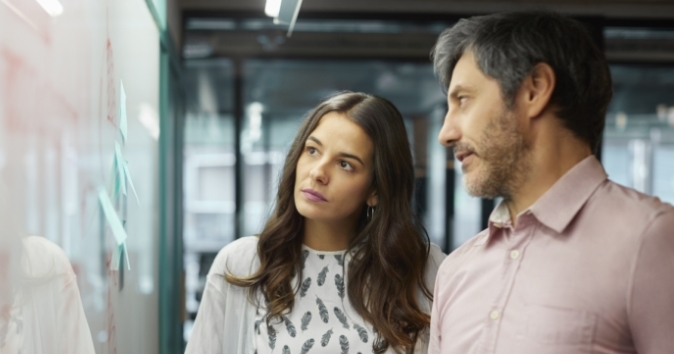 two coworkers, a woman and man, looking at a board with post-it notes reviewing the talent marketplace at their organization.