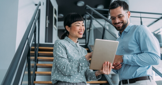 Two people in an office on a stairway looking at a tablet.