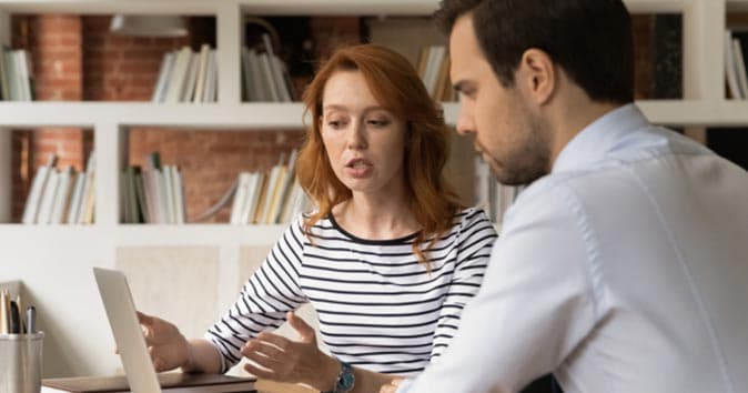 Men and women sitting at desks and looking at the laptop.