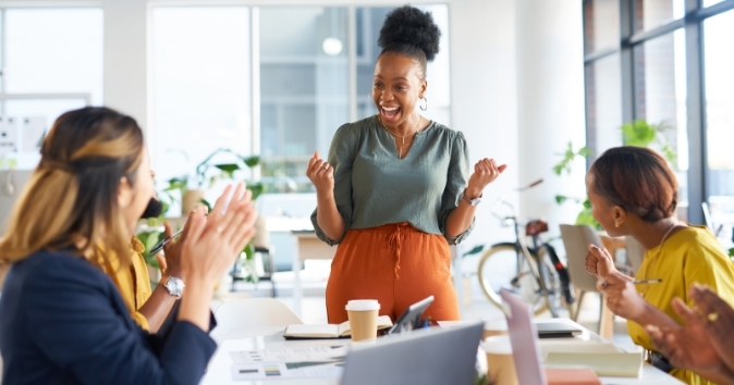 Woman with a big smile and co-workers clapping in an office.