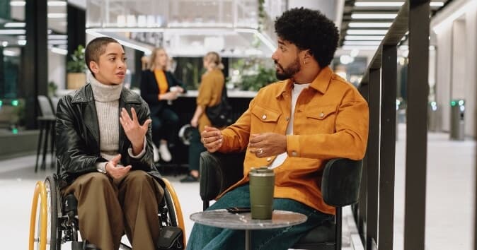 Woman in wheelchair speaking to man sitting next to her.