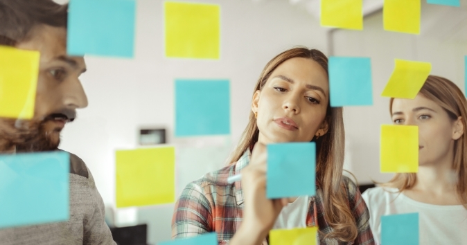 Woman writing on a post-it on a glass wall.