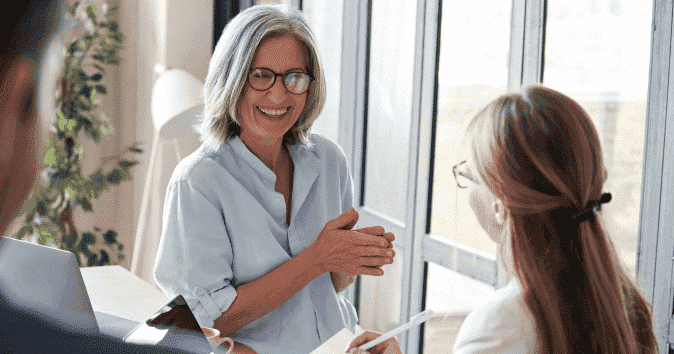 Happy-old-female-mentor-help-employees-at-group-office-meeting