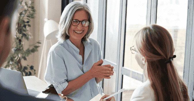 Happy-old-female-mentor-help-employees-at-group-office-meeting
