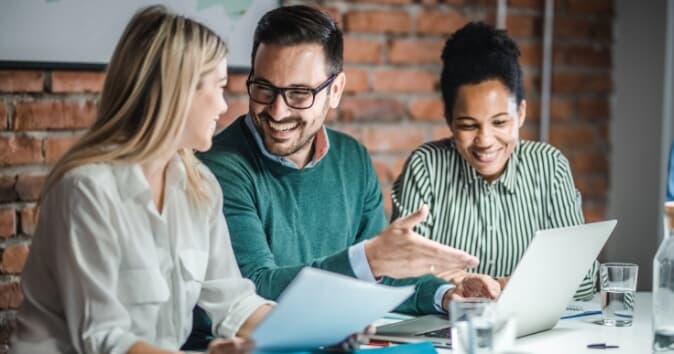 Three people at a table in an office smiling.