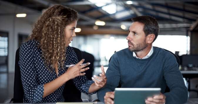 A woman and man talking at a desk.