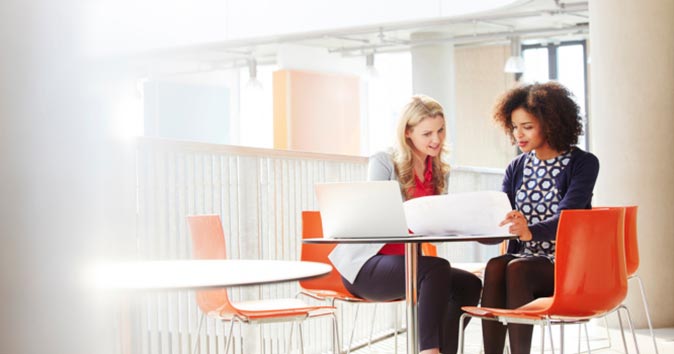 Two women sitting at the table and looking at the paper.