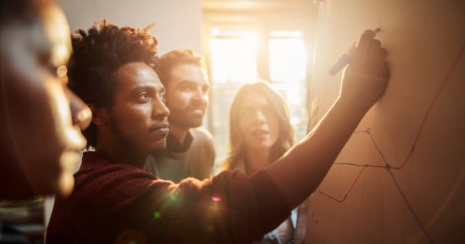 Room of people working on a whiteboard with the sun coming in from the windows.