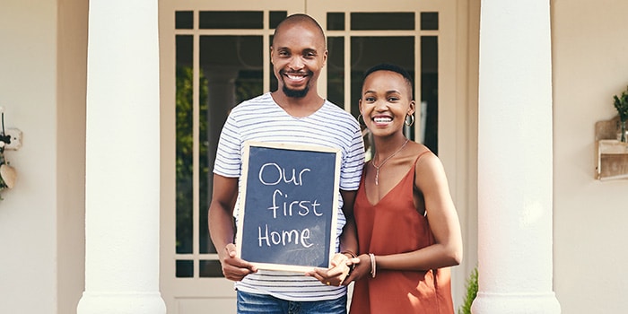 a couple stand in front of a house with a sign that reads "our first home"
