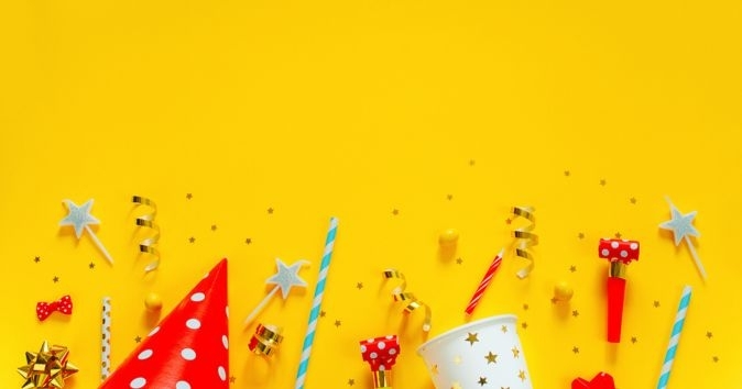 candles, ribbons, party hats and cups on a yellow background