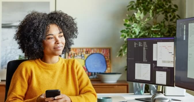 Woman on phone looking at a computer screen in her home office.