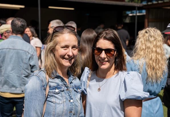 Man writes on sticky note posted on glass wall in focus with a woman smiling out of focus.