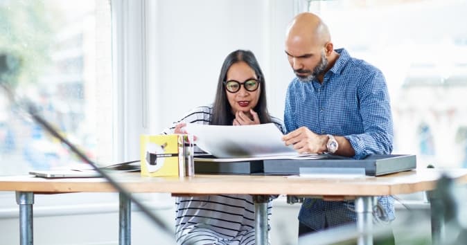 Two people looking over a piece of paper in an office at a desk.