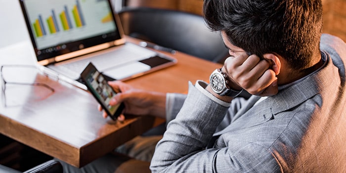 bored man on his phone in front of work laptop