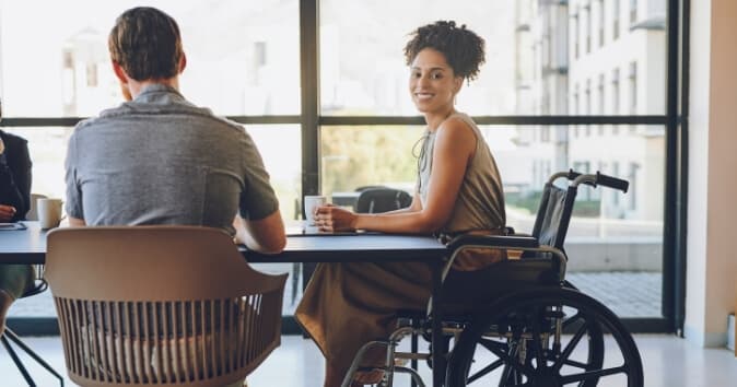 Woman in wheelchair at a table with a man in a seat.